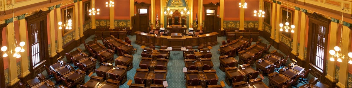 A grand hall with ornate chandeliers, a central aisle, and rows of wooden desks.