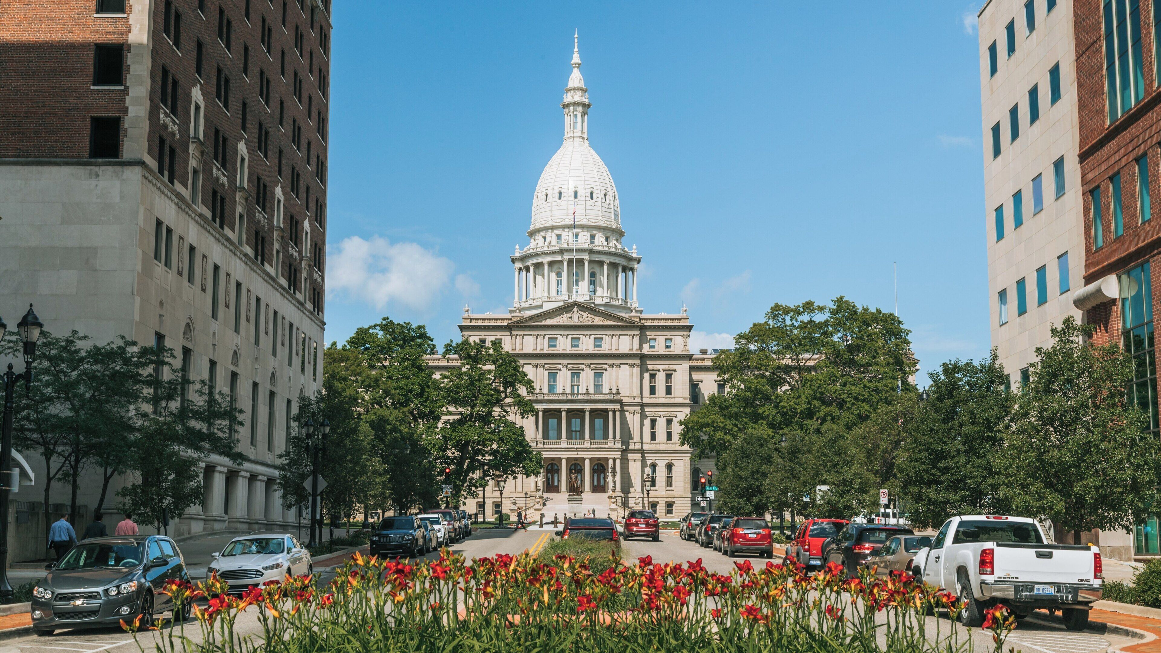 View of Michigan State Capitol surrounded by vibrant flowers and city buildings in downtown Lansing