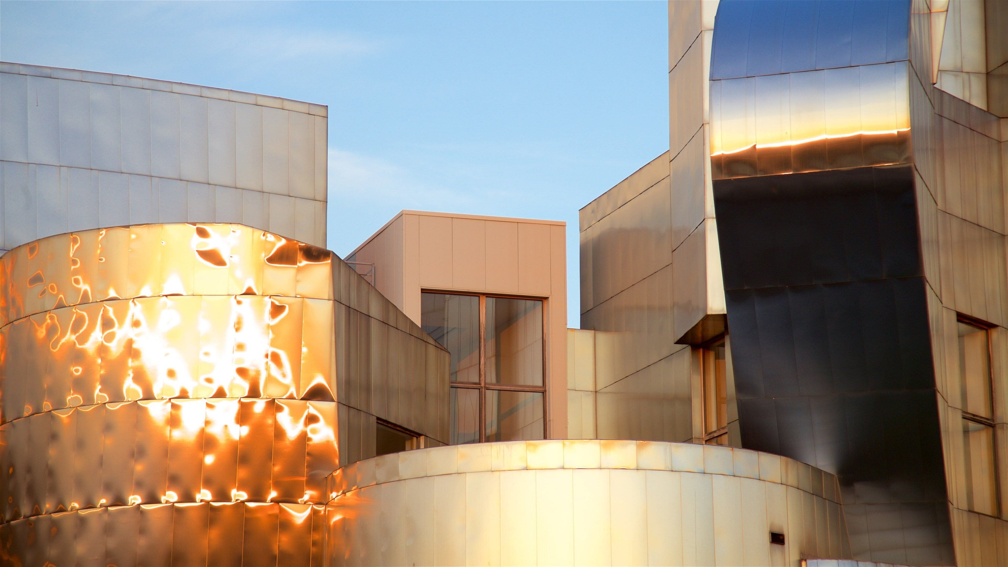 A modern building with reflective metallic surfaces and a large cylindrical structure with illuminated patterns.