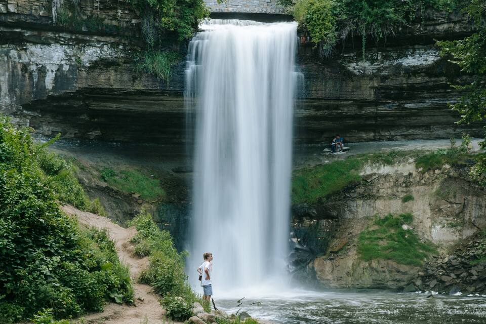 A waterfall cascading down a rocky cliff surrounded by lush greenery.