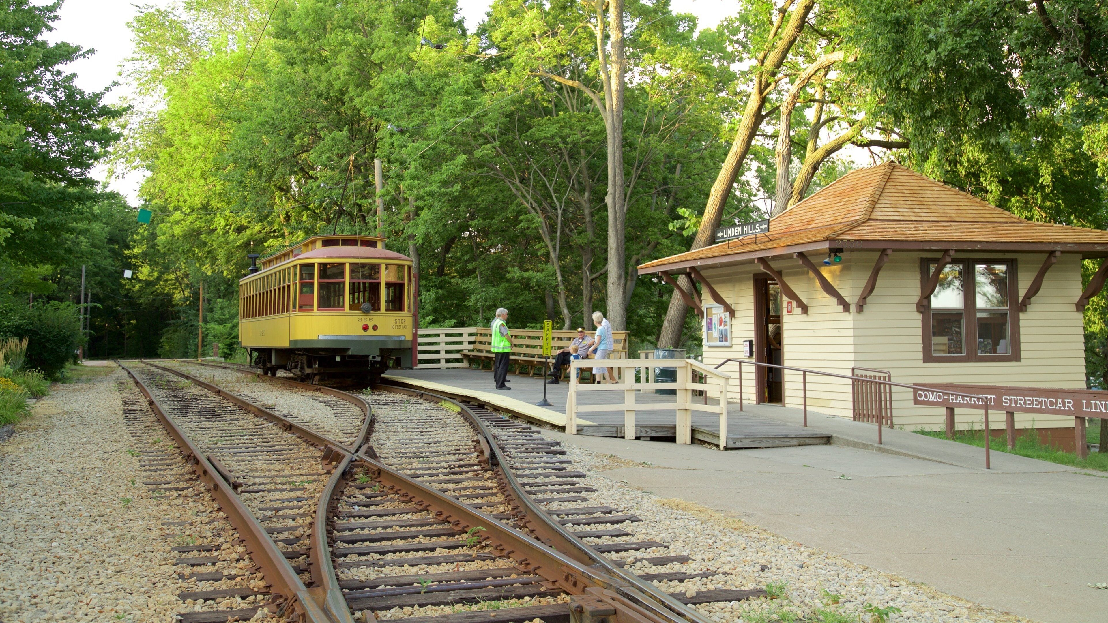 A vintage streetcar at a station surrounded by lush greenery.