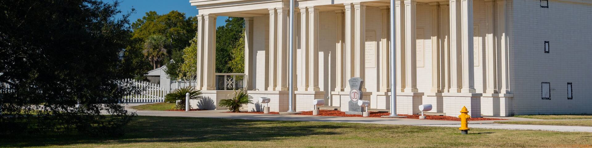 Un bâtiment blanc orné de colonnes, avec deux drapeaux et une horloge.