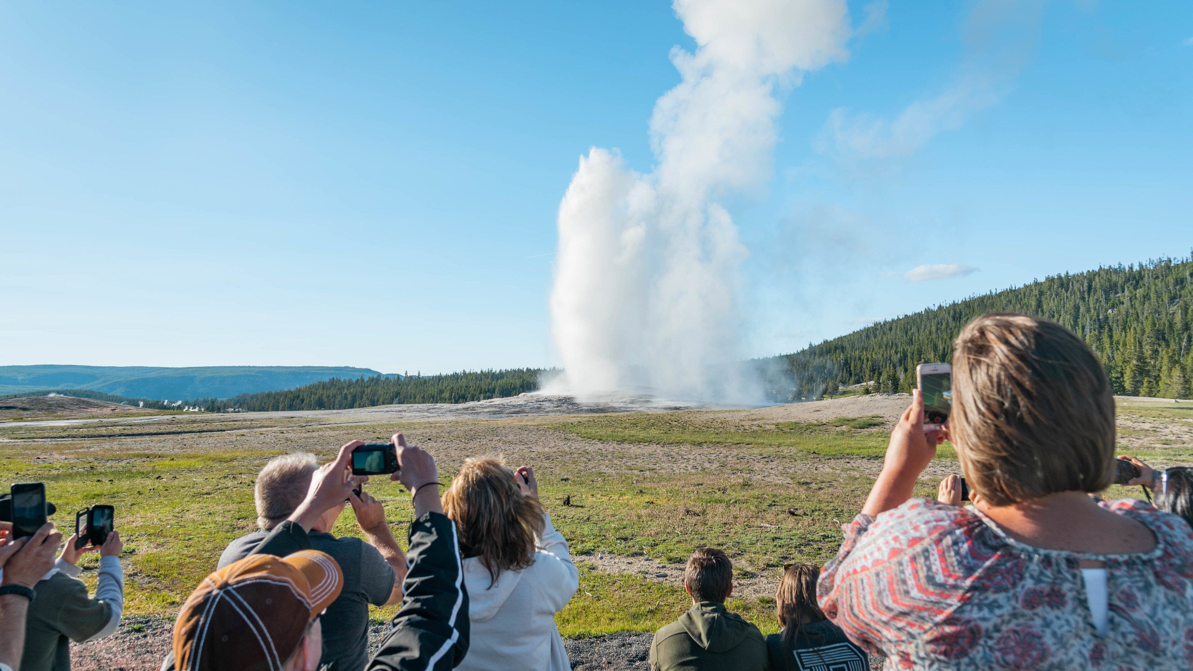 Old Faithful featuring a hot spring and mist or fog as well as a small group of people