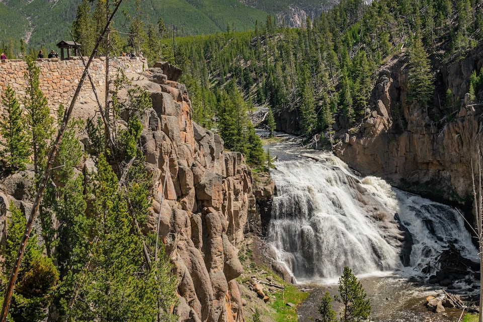 Une cascade se déversant le long d’une falaise rocheuse, entourée d’une forêt dense.
