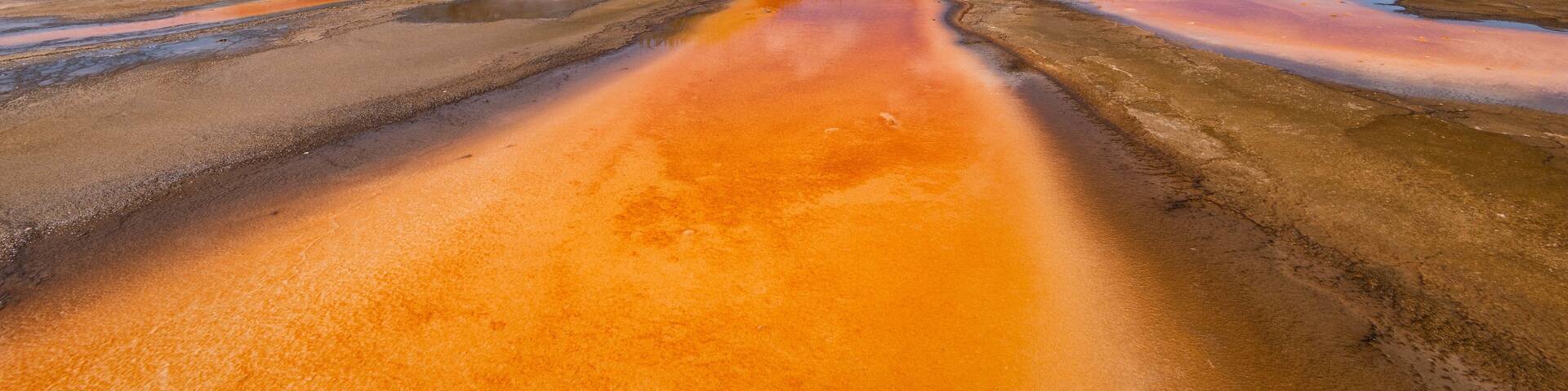 A geothermal area with colorful mineral deposits and steam rising from the ground.