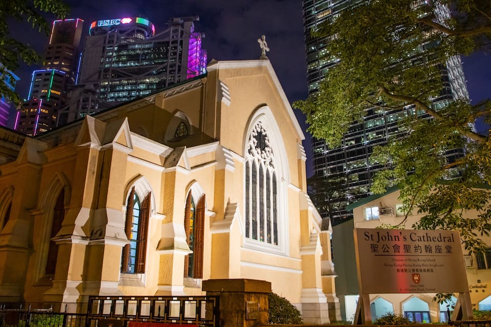 St John's Cathedral with Gothic architecture, surrounded by modern skyscrapers and illuminated signs.