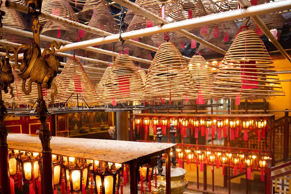 A temple interior with hanging incense burners and red lanterns.