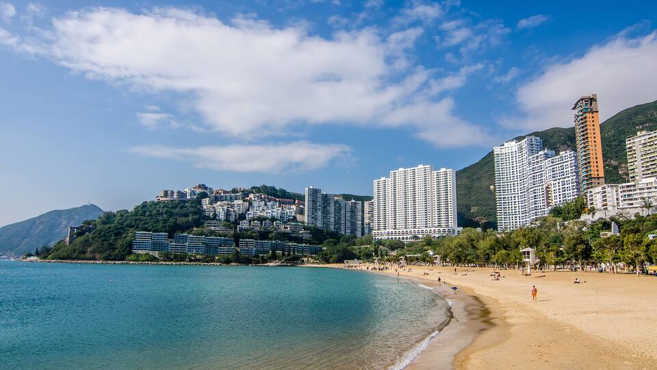 A coastal cityscape with a beach, high-rise buildings, and a mountain backdrop.