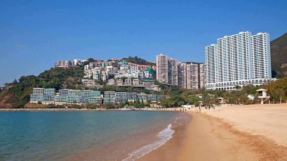 A coastal cityscape with a beach, high-rise buildings, and a hilly backdrop.