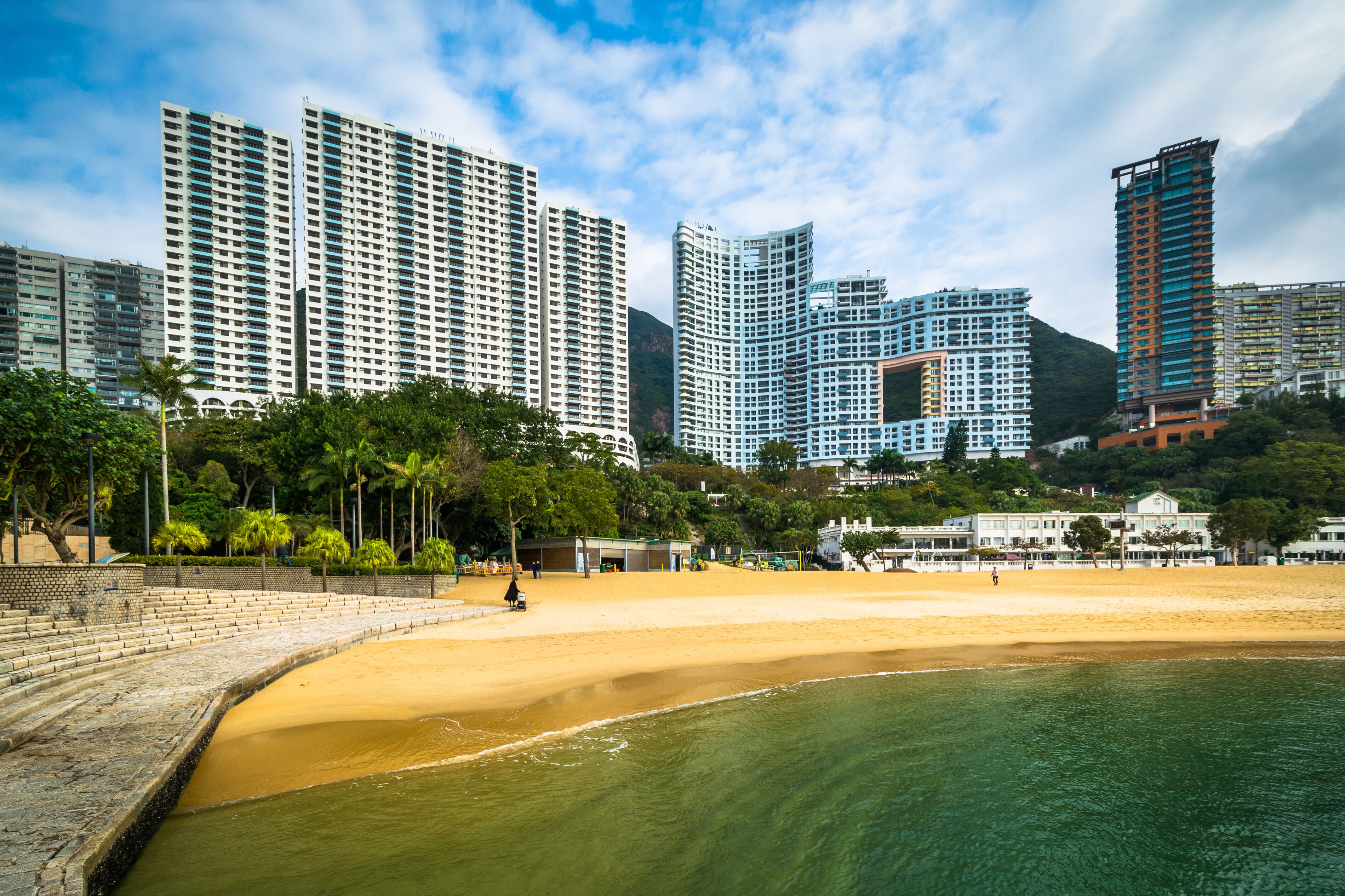 Paisagem costeira com edifícios altos, uma praia de areia e um mar calmo.