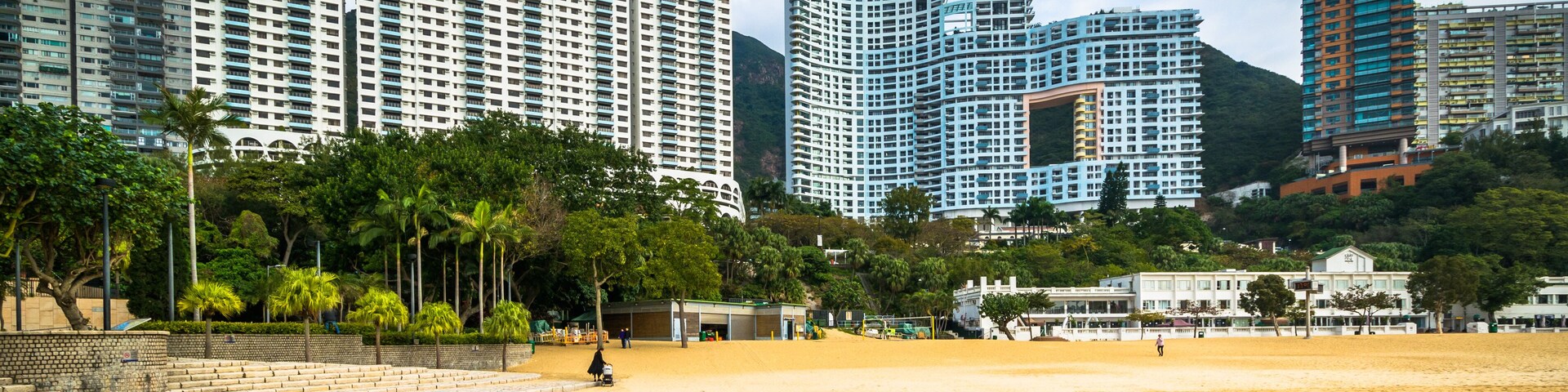 Paisagem costeira com edifícios altos, uma praia de areia e um mar calmo.