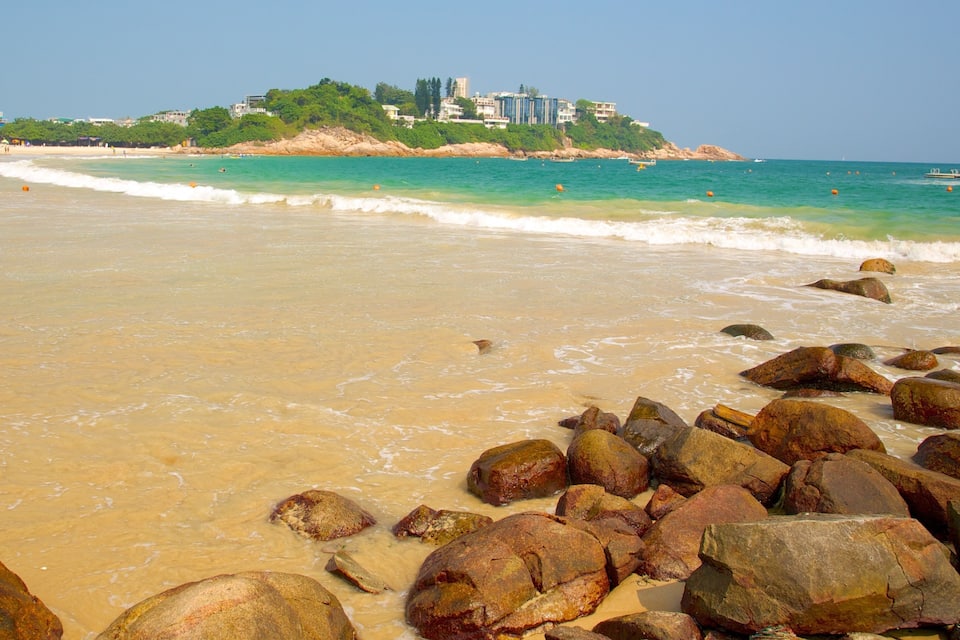 A beach with large rocks in the foreground and a cityscape in the background.