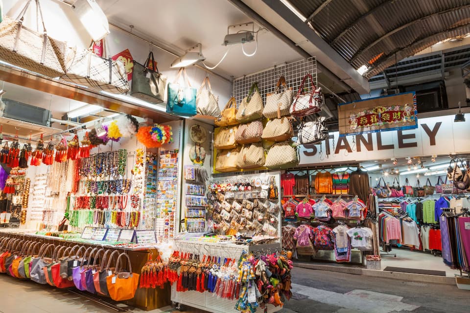 A busy market with various stalls selling bags, jewelry, and clothing.