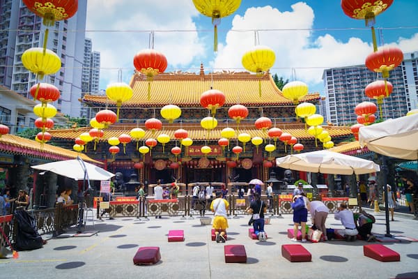 Un temple chinois traditionnel, doté d’une architecture richement décorée, de lanternes rouges et jaunes, et où l’on peut voir des gens.