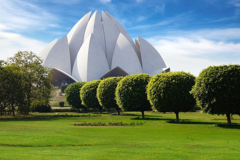 A modern architectural structure with a lotus-like design, surrounded by well-maintained green lawns and neatly trimmed trees.
