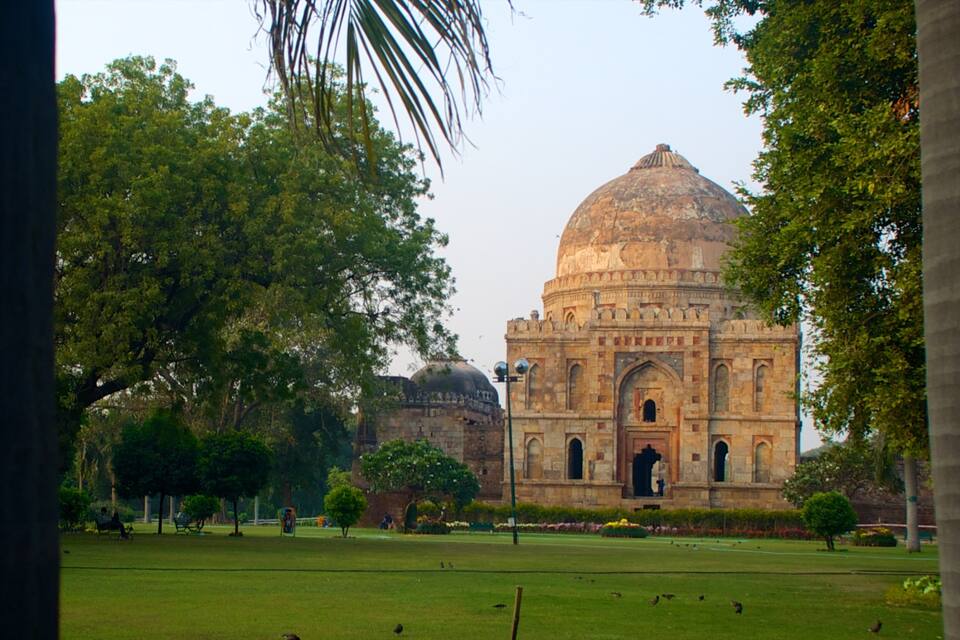 Um edifício grande e histórico com uma cúpula, rodeado por árvores verdes exuberantes e um jardim bem cuidado.