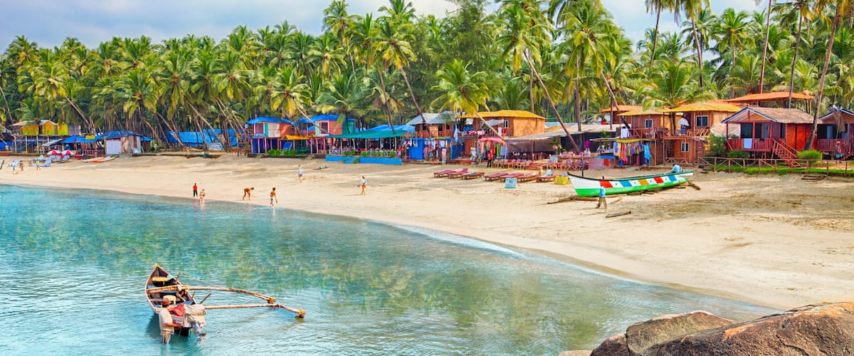 A beach with clear turquoise water, a small boat, and palm trees.