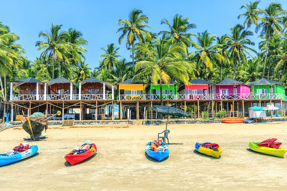 Colorful beach huts, palm trees, and kayaks on a sandy beach.