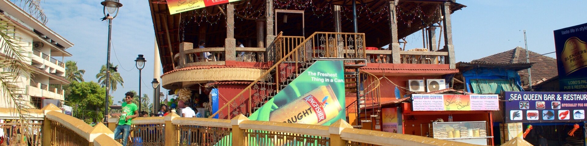 Un restaurante frente al agua con terraza y un gran anuncio de cerveza Kingfisher.