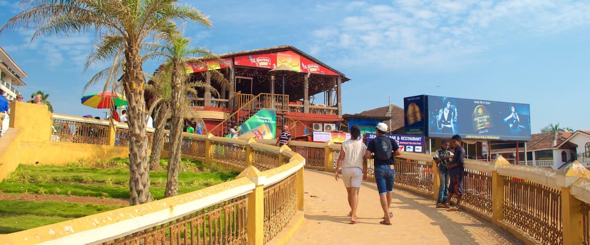 A pedestrian bridge with palm trees, a building with a red roof, and a billboard.