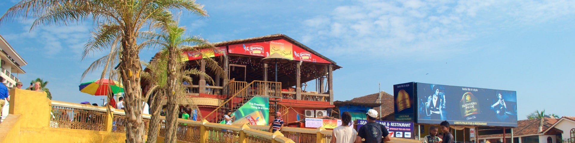 A pedestrian bridge with palm trees, a building with a red roof, and a billboard.