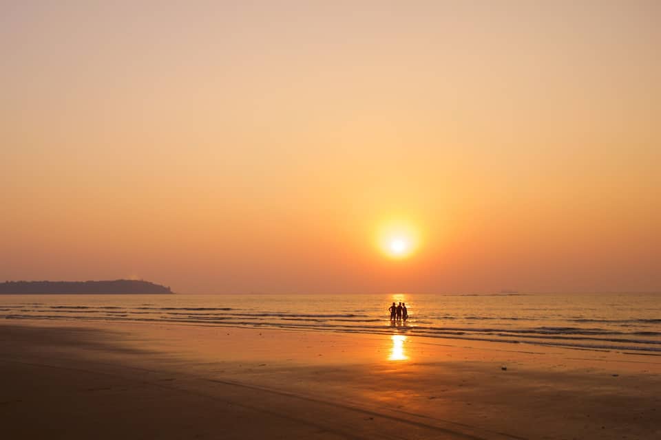 A beach at sunset with a group of people standing on the shore.