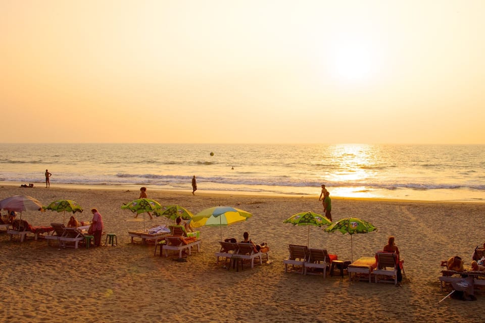 Una playa al atardecer con gente relajándose bajo sombrillas y tumbonas.