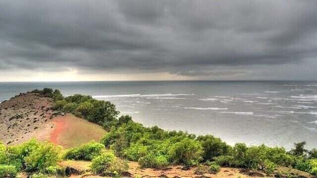 A coastal landscape with a beach, ocean, and overcast sky.