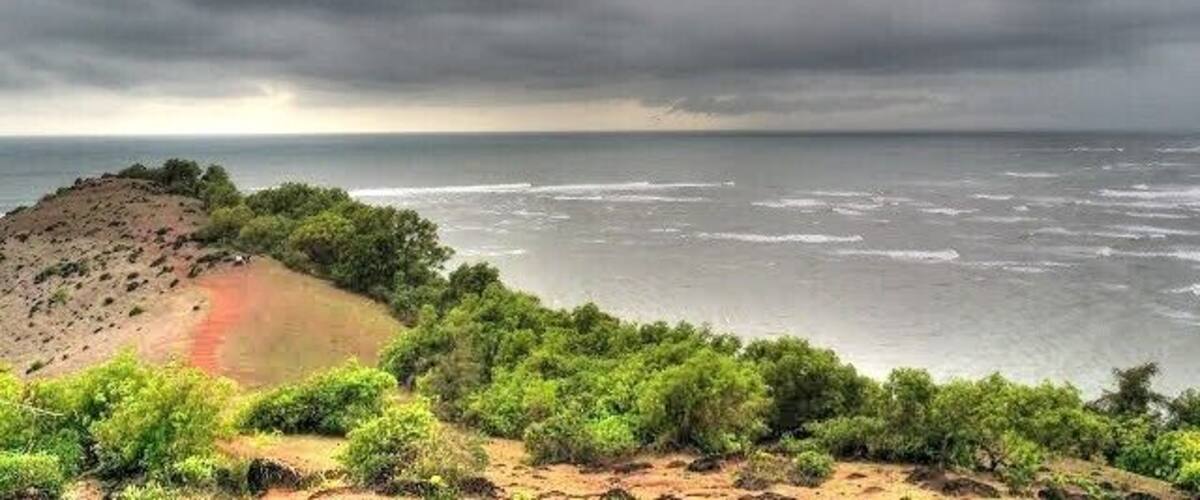 A coastal landscape with a beach, ocean, and overcast sky.