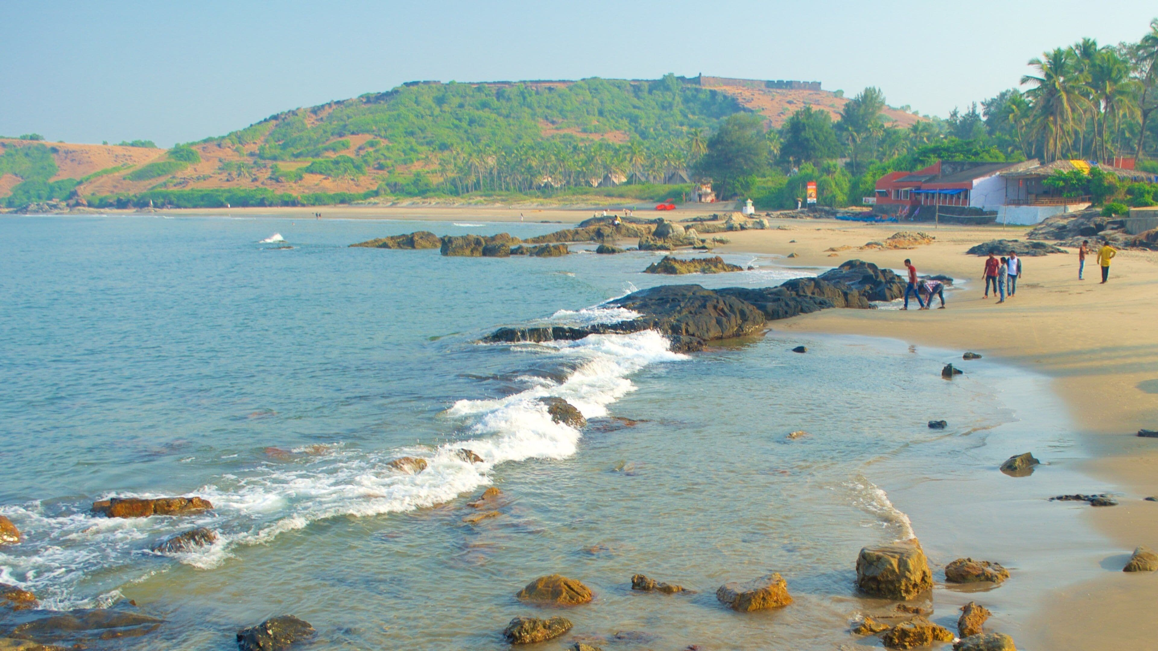 A beach with rocky shoreline, clear water, and a hill with vegetation in the background.