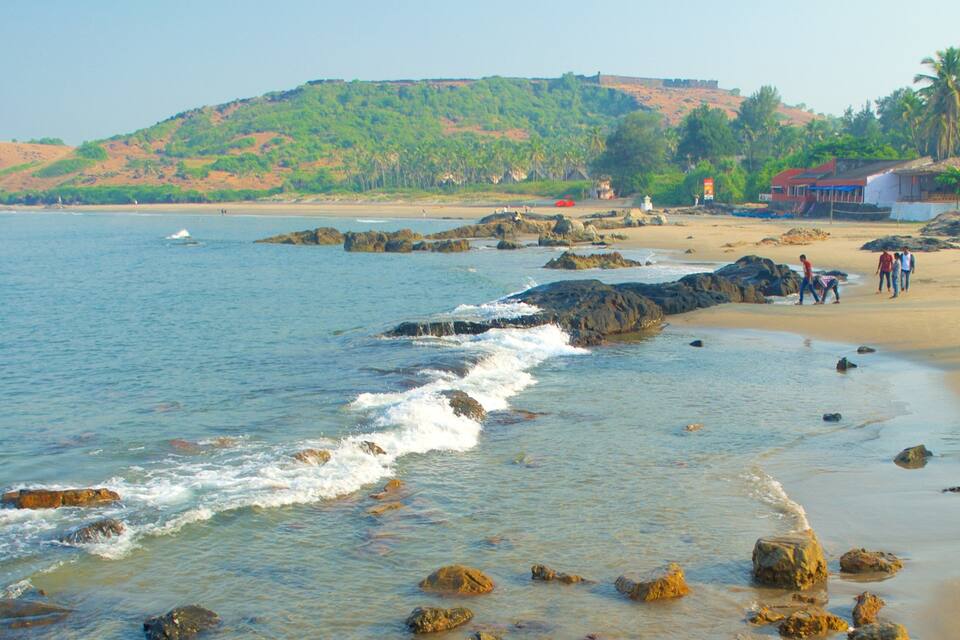 Una playa con costa rocosa, agua cristalina y una colina con vegetación al fondo.
