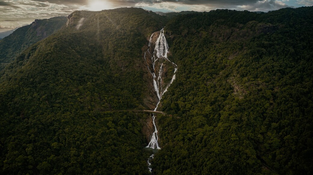 Aerial view of Dudhsagar Falls cascading through dense tropical forest under a dramatic cloudy sky at sunset Sonauli, Goa, India.