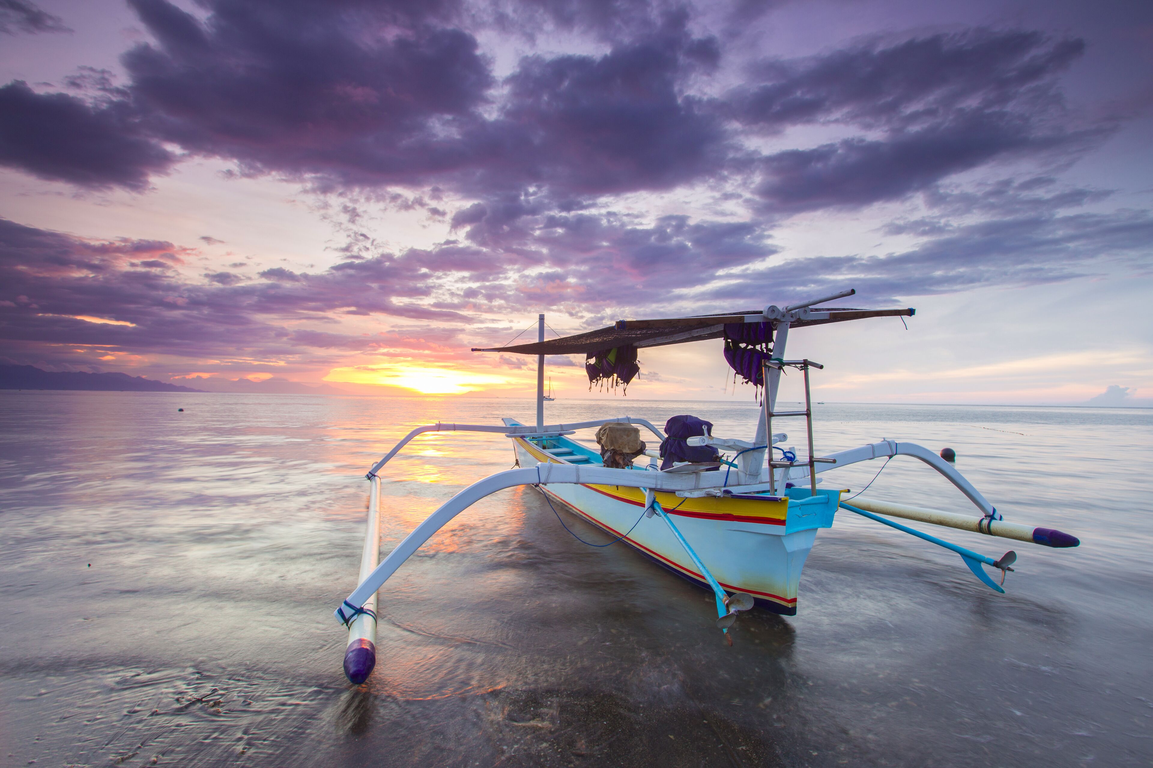 A traditional boat with a colorful design, anchored on calm water during sunset.