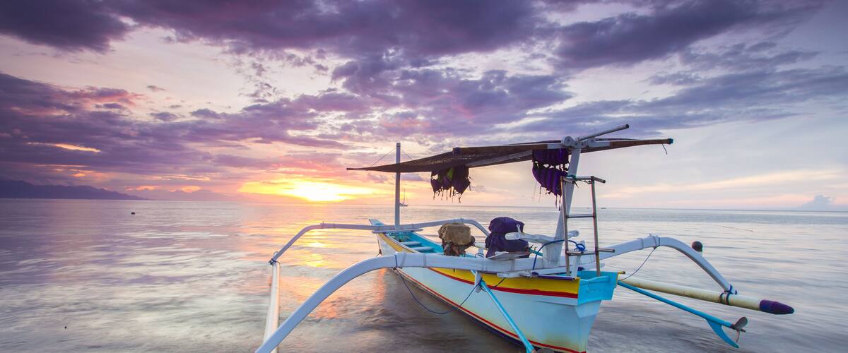 A traditional boat with a colorful design, anchored on calm water during sunset.