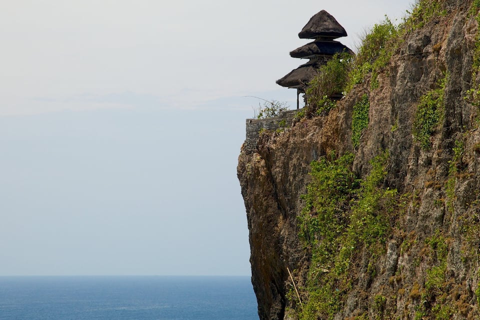 Um penhasco com uma construção tradicional de telhado de colmo no topo.