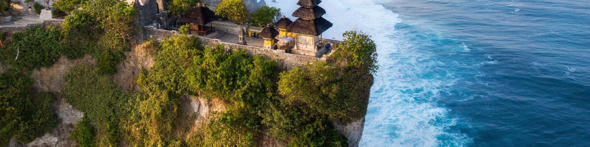 A coastal cliffside with a traditional thatched-roof structure overlooking the ocean.