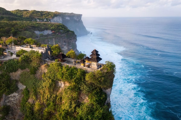 A coastal cliffside with a traditional thatched-roof structure overlooking the ocean.