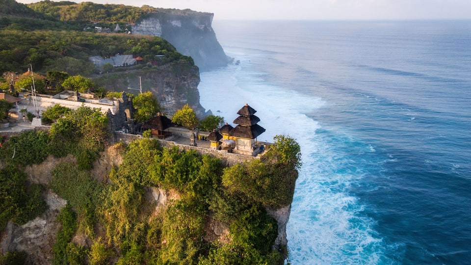 A coastal cliffside with a traditional thatched-roof structure overlooking the ocean.