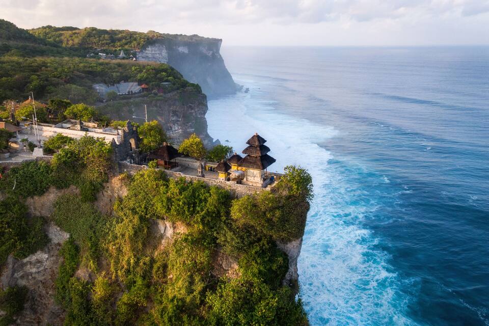 A coastal cliffside with a traditional thatched-roof structure overlooking the ocean.