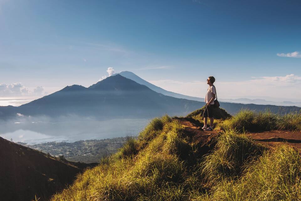 A person standing on a grassy hill overlooking a mountain and a valley.