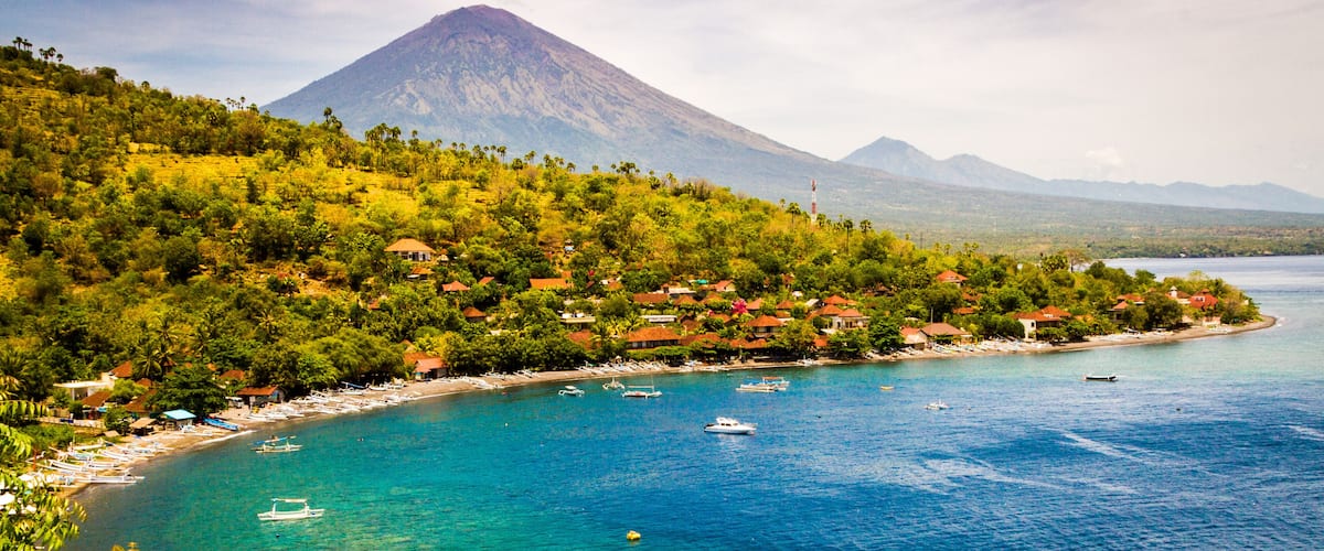 A coastal town with a mountain in the background, clear blue waters, and boats.