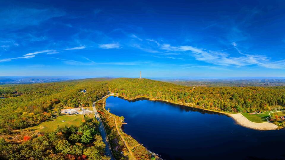 A lake surrounded by forest, a lighthouse, and a distant mountain range.