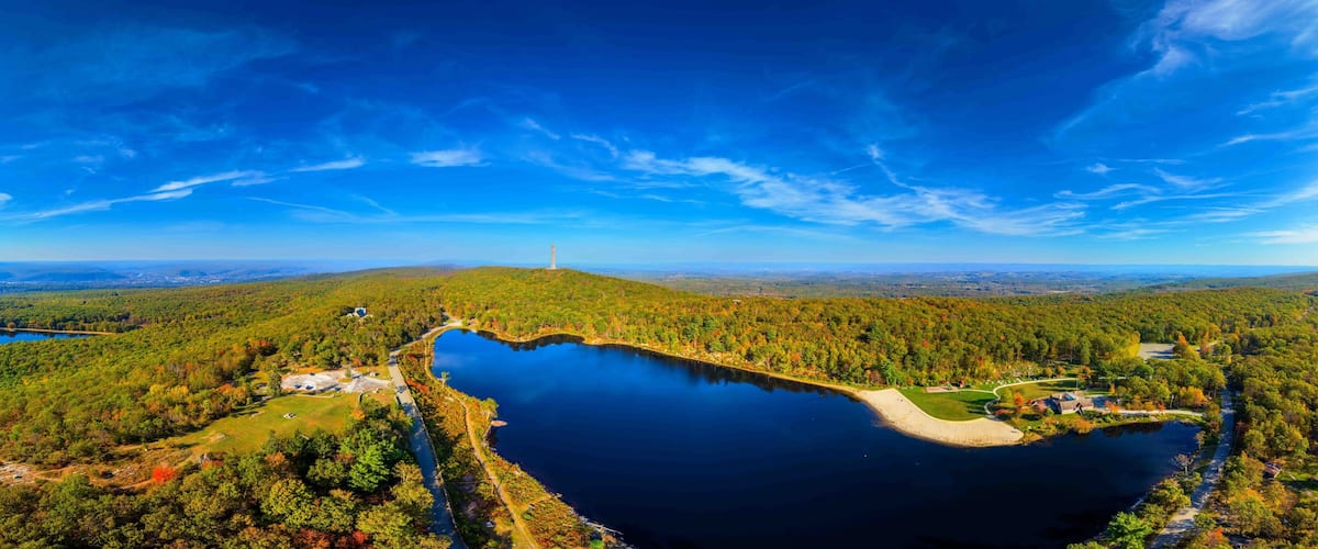 A lake surrounded by forest, a lighthouse, and a distant mountain range.