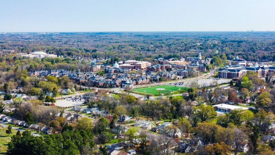 A university campus with historic buildings, a large green field, and surrounding residential areas.