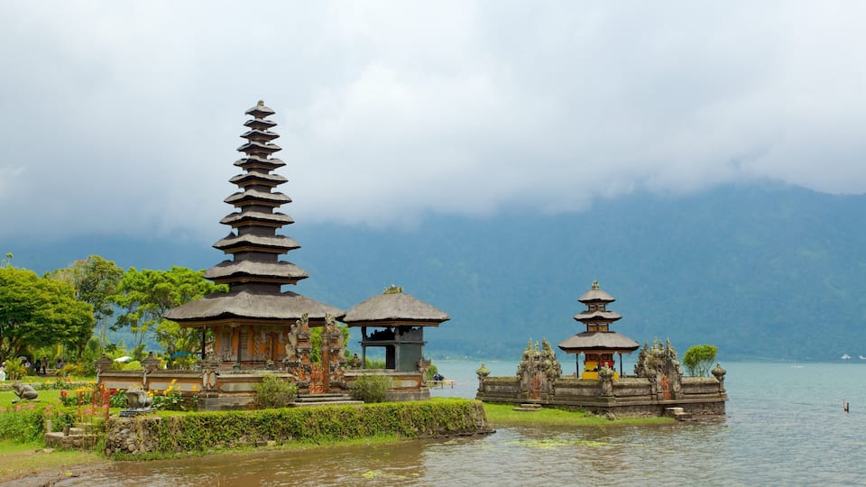 A serene temple complex by a lake with tiered pagodas and a thatched-roof structure.