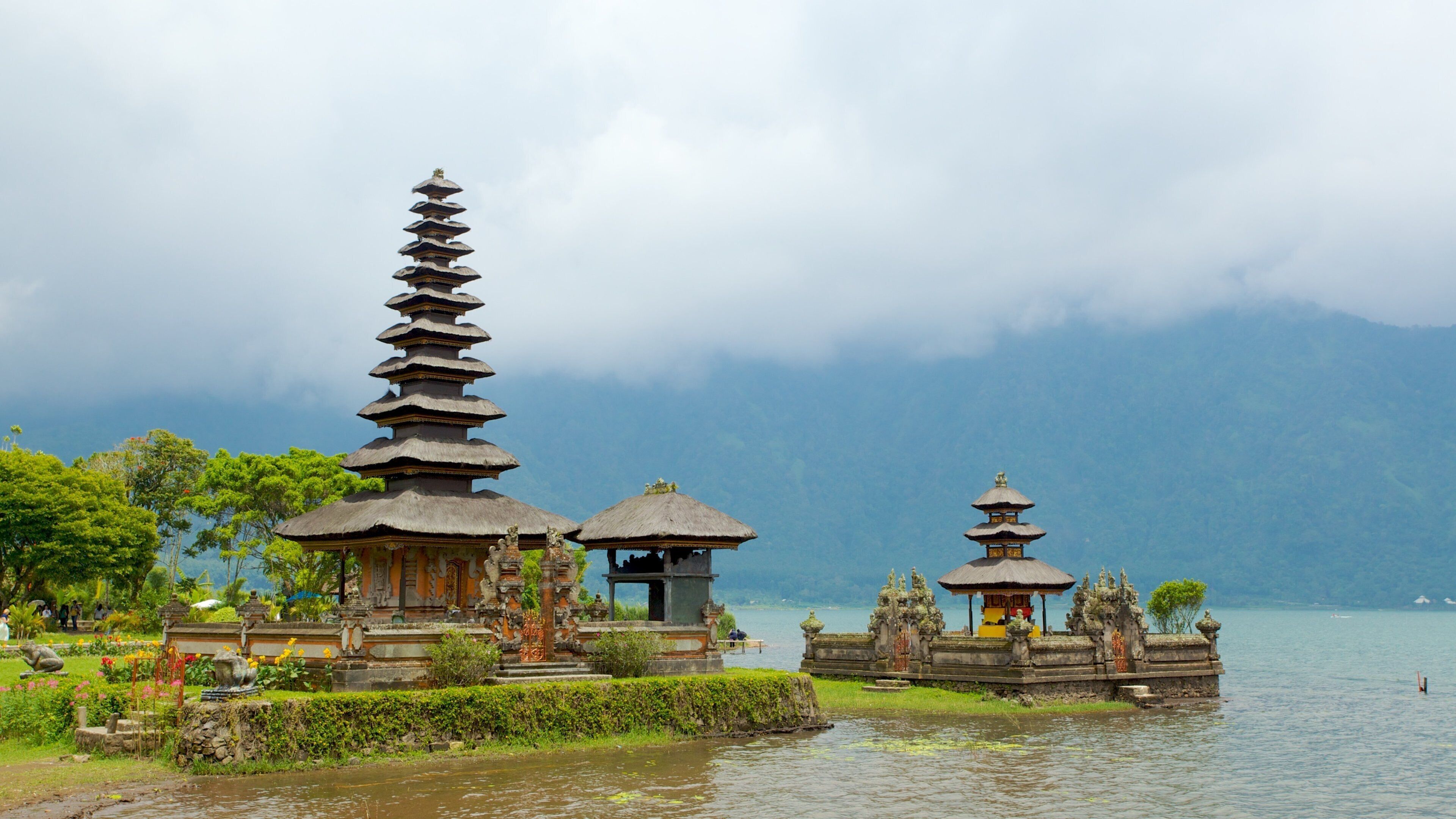 A serene temple complex by a lake with tiered pagodas and a thatched-roof structure.