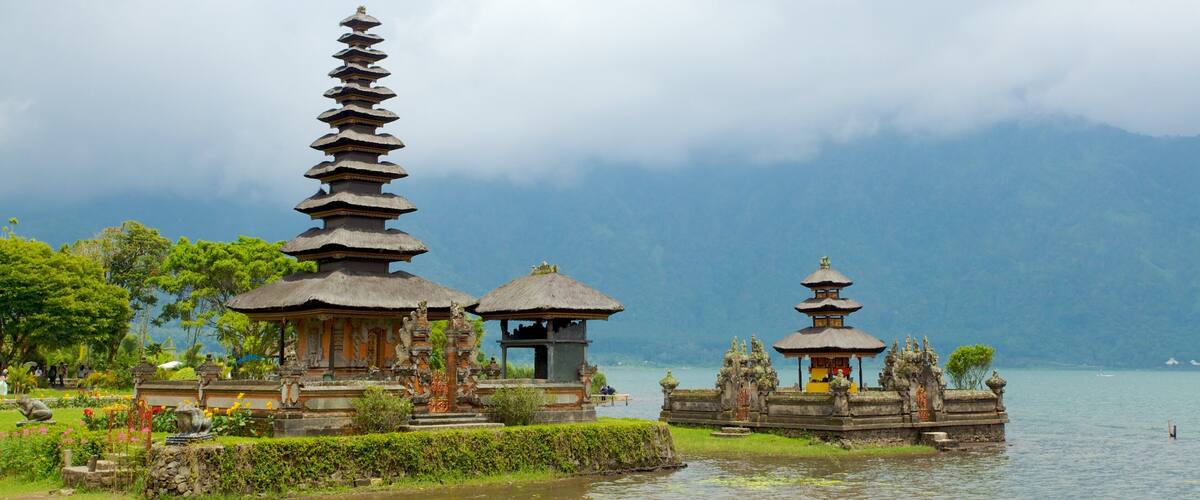 A serene temple complex by a lake with tiered pagodas and a thatched-roof structure.