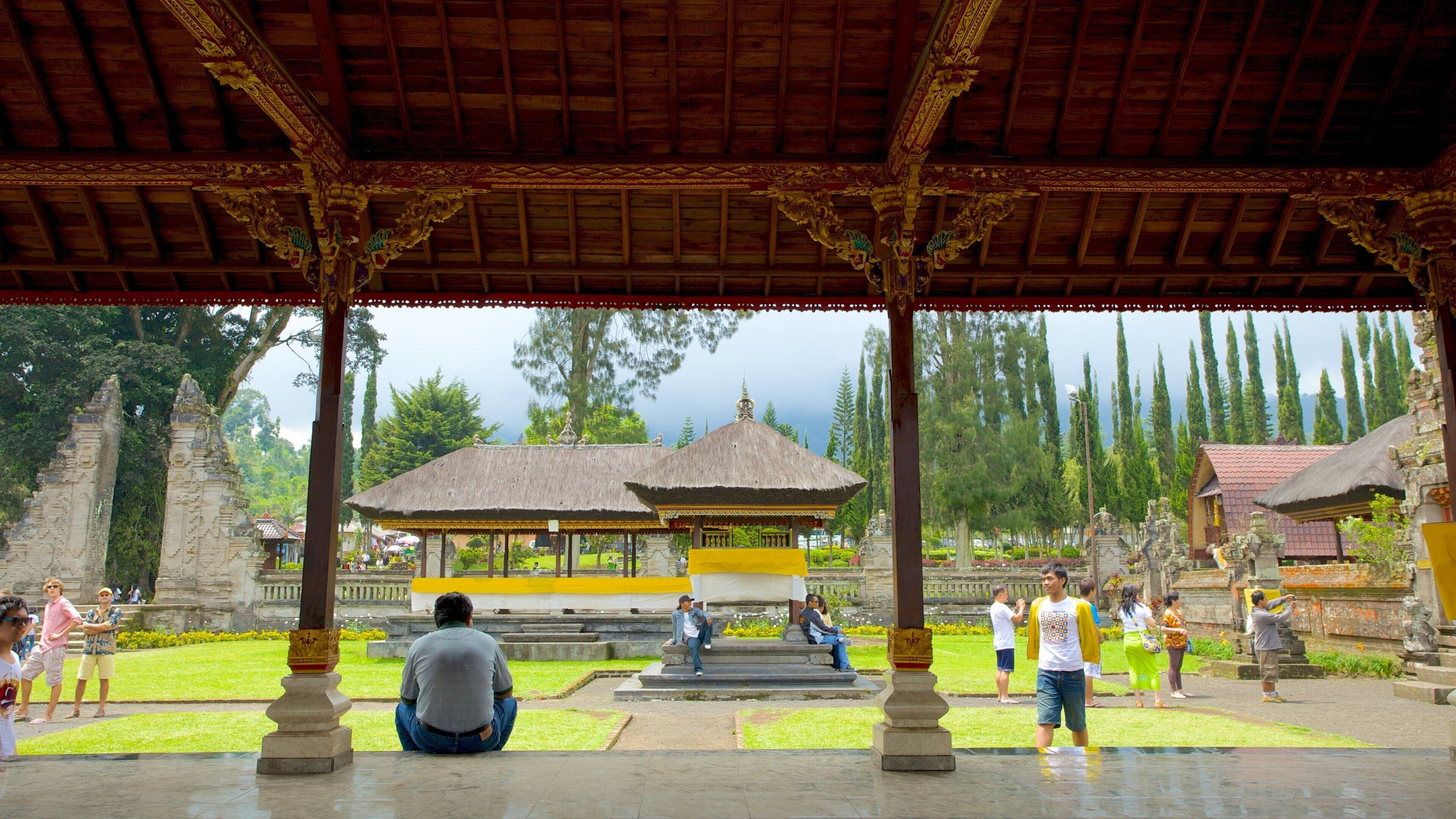 A traditional pavilion with ornate pillars and a thatched roof, surrounded by lush greenery and ancient stone structures.