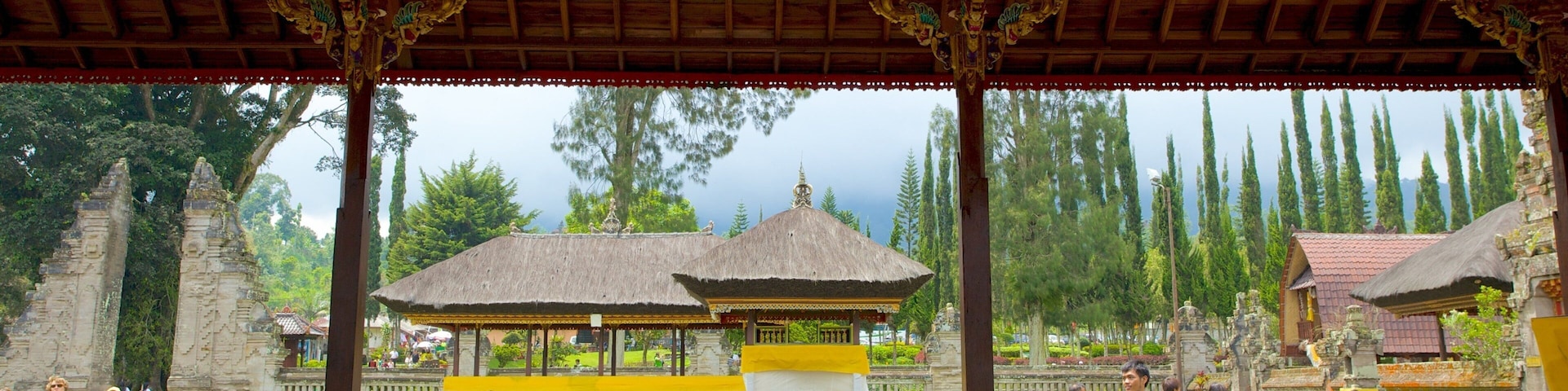 A traditional pavilion with ornate pillars and a thatched roof, surrounded by lush greenery and ancient stone structures.