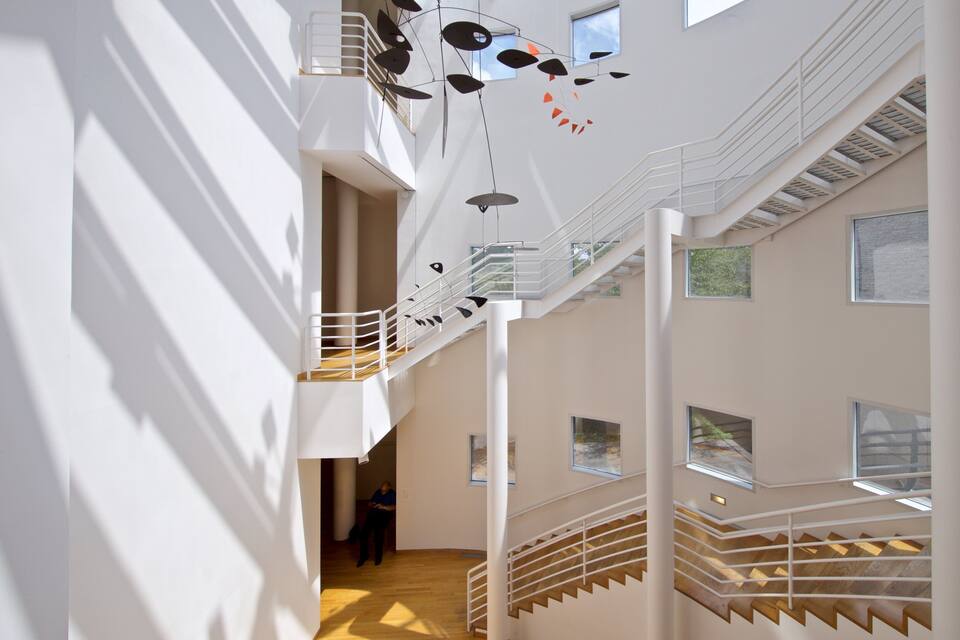 A modern interior with a wooden staircase, white walls, and hanging abstract art.
